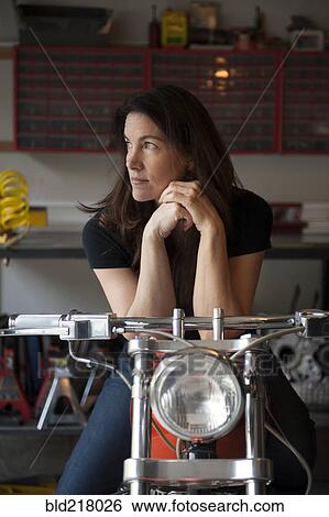 Stock Photograph - Woman sitting on motorcycle in garage. Fotosearch