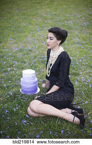 Picture - Woman sitting with cake in rural field. Fotosearch