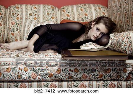 Stock Image - Woman sitting with oversized book on sofa. Fotosearch