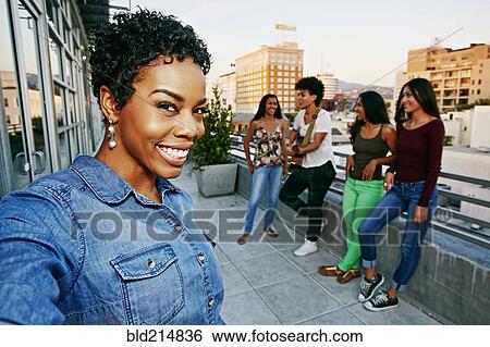 Stock Photograph - Woman smiling with friends on urban rooftop. Fotosearch