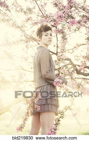 Stock Image - Woman standing in flowering trees. Fotosearch