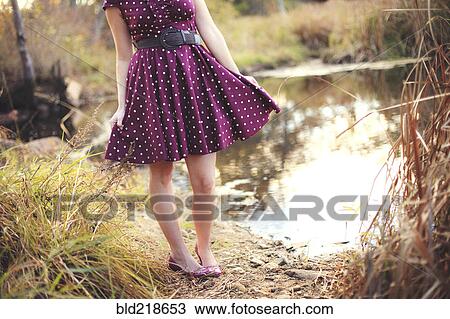 Stock Image - Woman standing near rural pond. Fotosearch