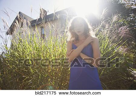 Stock Photography - Woman standing near tall plants in backyard. Fotosearch