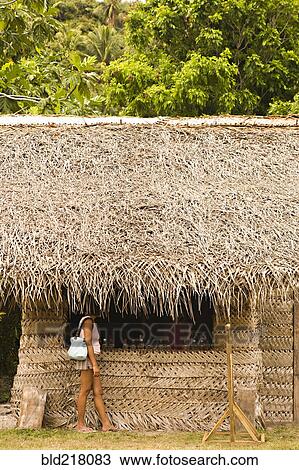 Stock Image - Woman standing under thatched hut roof. Fotosearch