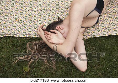 Stock Photograph - Woman sunbathing in bikini on blanket in grass. Fotosearch