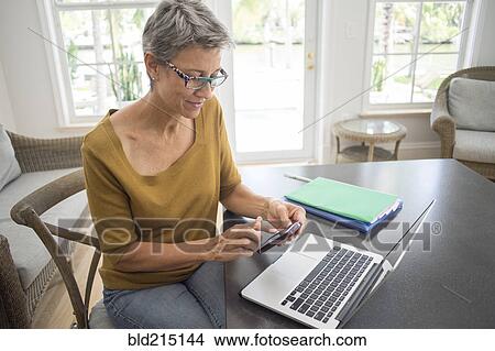 Woman using cell phone and laptop in living room View Large Photo Image Picture - Woman using cell phone and laptop in living room. Fotosearch