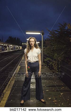 Stock Image - Woman waiting for train at train station at night. Fotosearch