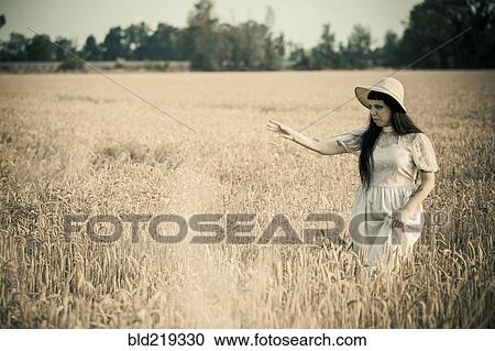 Stock Image - Woman walking in tall grass in rural field. Fotosearch