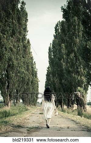 Stock Image - Woman walking on dirt road. Fotosearch