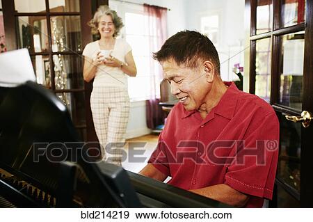 Stock Photo - Woman watching husband playing piano in living room. Fotosearch