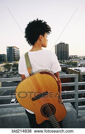 Stock Photo - Woman wearing guitar on urban rooftop. Fotosearch