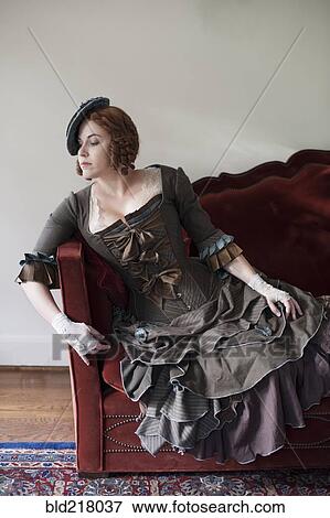 Stock Photo - Woman wearing vintage gown and hat on sofa. Fotosearch