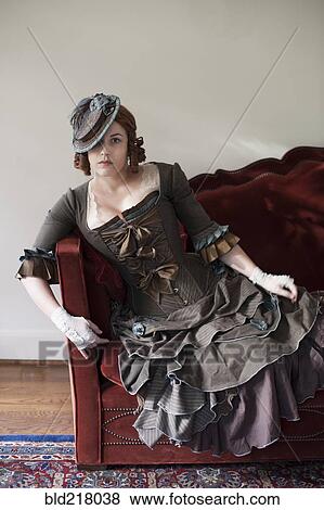 Stock Photo - Woman wearing vintage gown and hat on sofa. Fotosearch