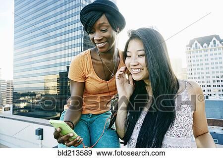 Stock Photo - Women listening to earbuds on urban rooftop. Fotosearch