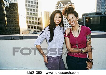 Stock Image - Women smiling on urban rooftop. Fotosearch