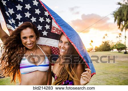 Stock Image - Women standing under American flag quilt at sunset. Fotosearch