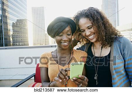 Stock Photo - Women using cell phone together on urban rooftop. Fotosearch