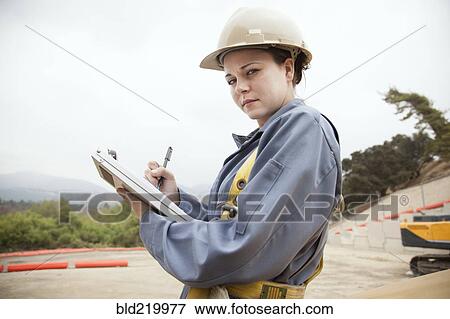 Stock Photo - Worker writing on clipboard at construction site. Fotosearch