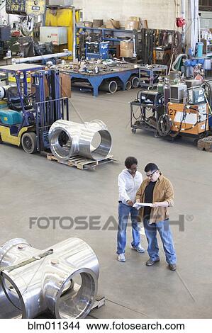 Picture - Workers looking at paperwork in factory. Fotosearch