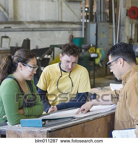 Stock Photo - Workers reviewing paperwork in factory. Fotosearch