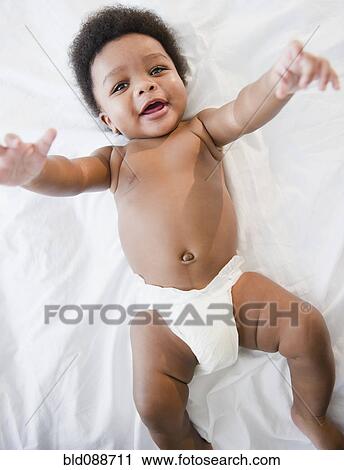 Stock Image - African American baby boy laying on bed. Fotosearch