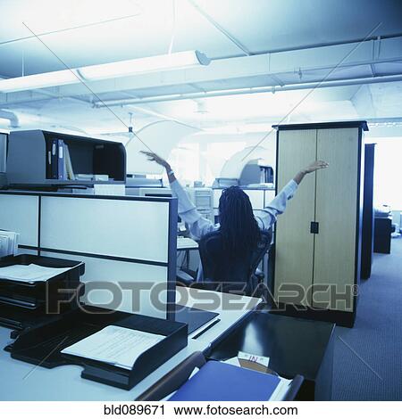 Stock Image - African American businesswoman stretching in office cubicle. Fotosearch
