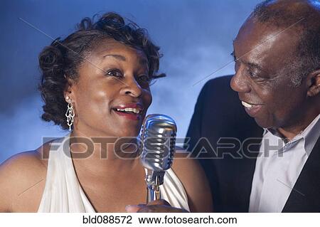 Stock Image - African American couple singing together into microphone. Fotosearch
