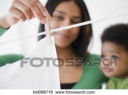 Stock Photograph - African American mother and son hanging clothing on clothes line. Fotosearch