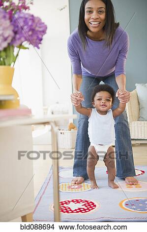 Picture - African American mother helping baby boy learn to walk. Fotosearch