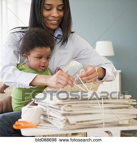 Stock Photo - African American mother holding baby on lap and tying newspapers. Fotosearch