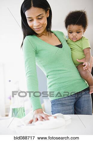 Stock Photo - African American mother holding baby boy and cleaning. Fotosearch