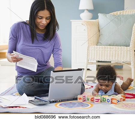African American mother working on laptop while baby plays on floor View Large Photo Image Stock Photograph - African American mother working on laptop while baby plays on floor. Fotosearch