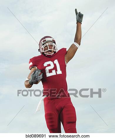 Stock Image - Black football player carrying football making number 1 gesture. Fotosearch