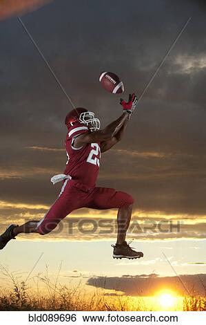 Stock Photograph - Black football player catching football player in mid-air. Fotosearch