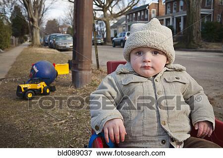 Boy in coat and cap sitting in yard View Large Photo Image Stock Photo - Boy in coat and cap sitting in yard. Fotosearch