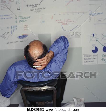 Stock Image - Businessman looking at drawings on office wall. Fotosearch