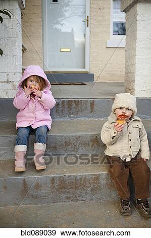 Stock Photo - Caucasian brother and sister eating cupcakes on front stoop. Fotosearch