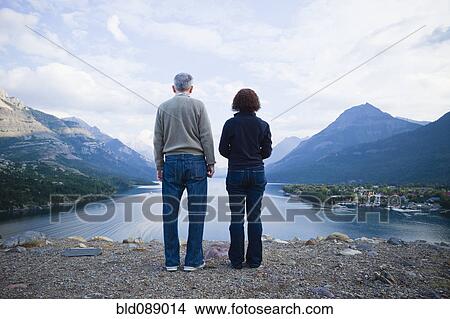 Picture - Caucasian couple standing outdoors with mountains in background. Fotosearch