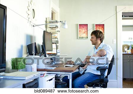 Stock Photo - Caucasian father working in home office and holding baby. Fotosearch