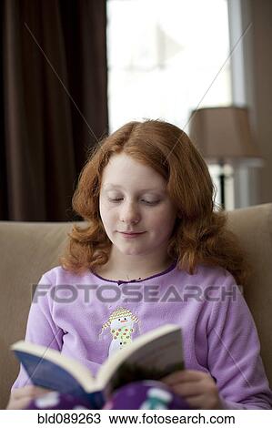 Stock Image - Caucasian girl on sofa reading book. Fotosearch