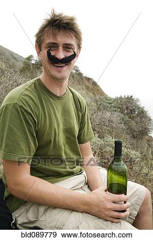 Stock Photo - Caucasian man in costume mustache holding wine bottle. Fotosearch