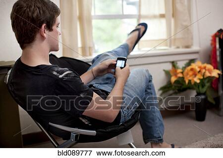 Stock Photo - Caucasian man text messaging on cell phone in dorm room. Fotosearch