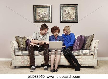 Stock Image - Caucasian mother and adult children using laptop together. Fotosearch