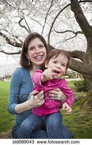 Stock Image - Caucasian mother and daughter sitting outdoors. Fotosearch