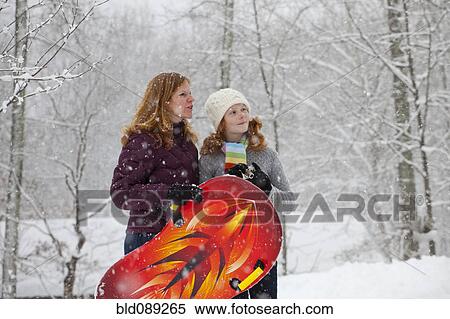 Stock Photography - Caucasian mother and daughter standing in snow with sled. Fotosearch