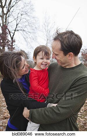 Stock Photograph - Caucasian parents holding daughter outdoors. Fotosearch