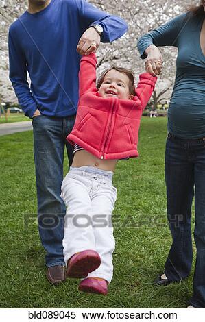 Stock Photography - Caucasian parents swinging daughter outdoors. Fotosearch