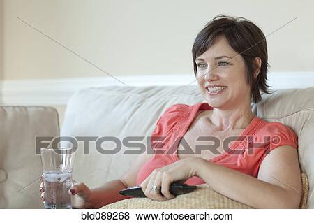 Stock Photo - Caucasian woman on sofa watching television. Fotosearch