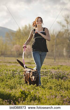 Stock Image - Caucasian woman running in field with dog. Fotosearch