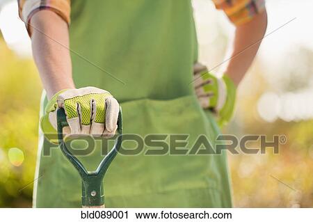 Stock Image - Caucasian woman standing with shovel in plant nursery. Fotosearch